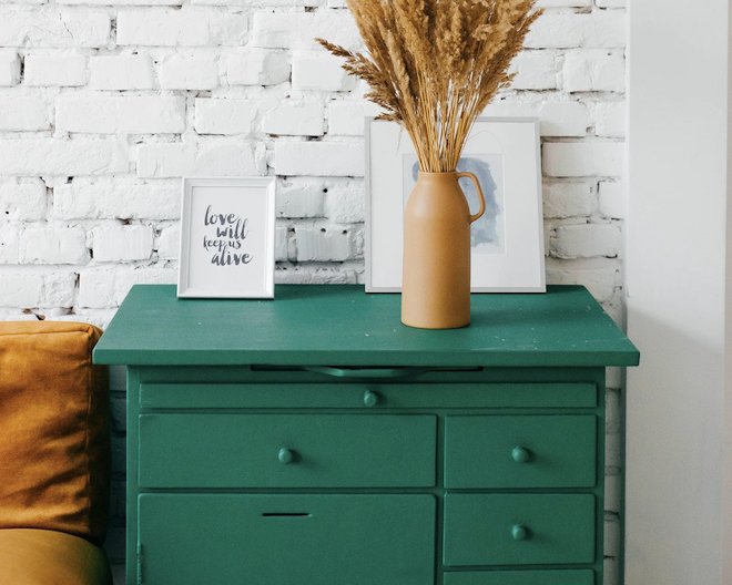 green side table with two pictures and a brass vase with wheat flowers.